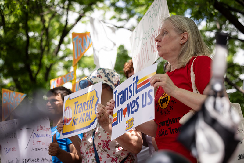 A woman in a crowd of ralliers holds a "transit moves us" sign