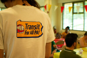 Someone wearing a white T shirt with the Transit for All PA! logo