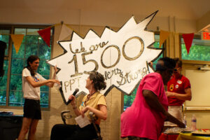 PPT staff making an announcement, 2 of them holding a huge, sparkly sign reading "we are 1500 PPT members strong!"
