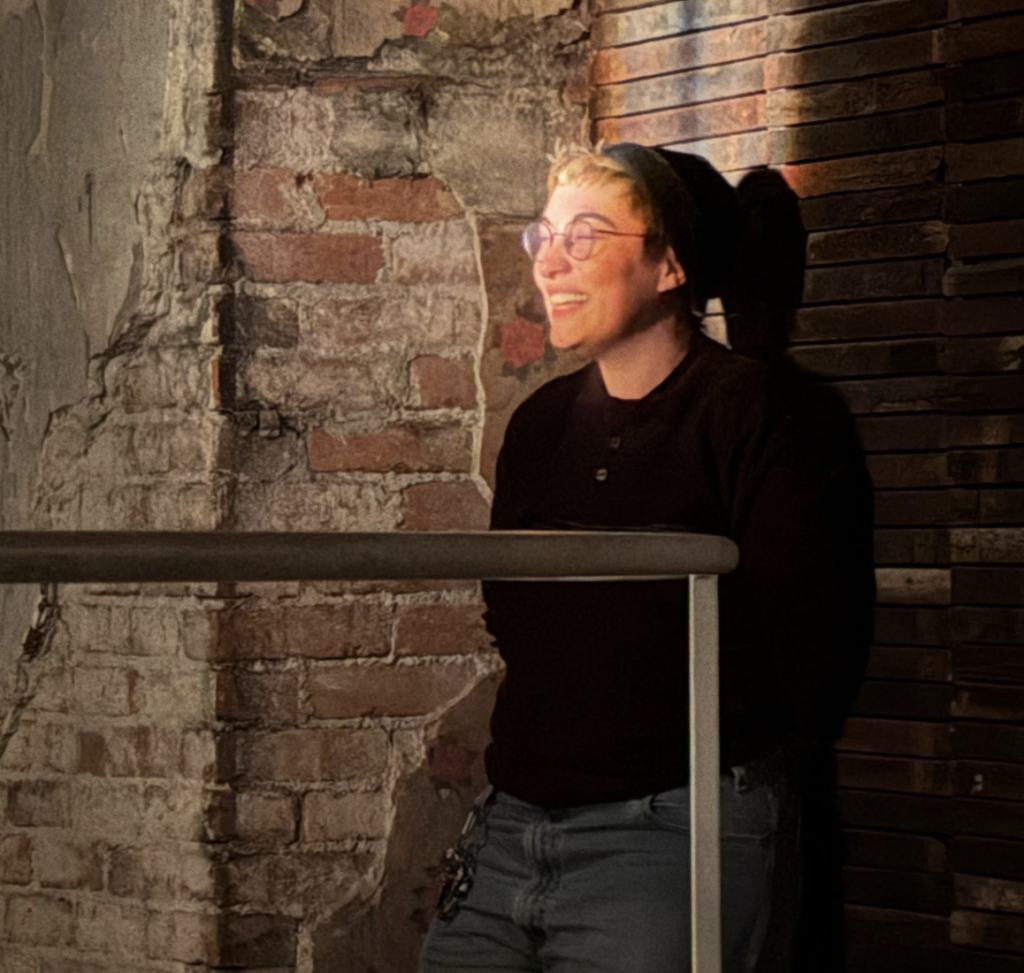 Ren Finkel smiles while standing against a sunny brick wall
