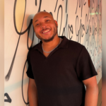 Kristopher Chandler, a Black man smiling against a wall with black and white art
